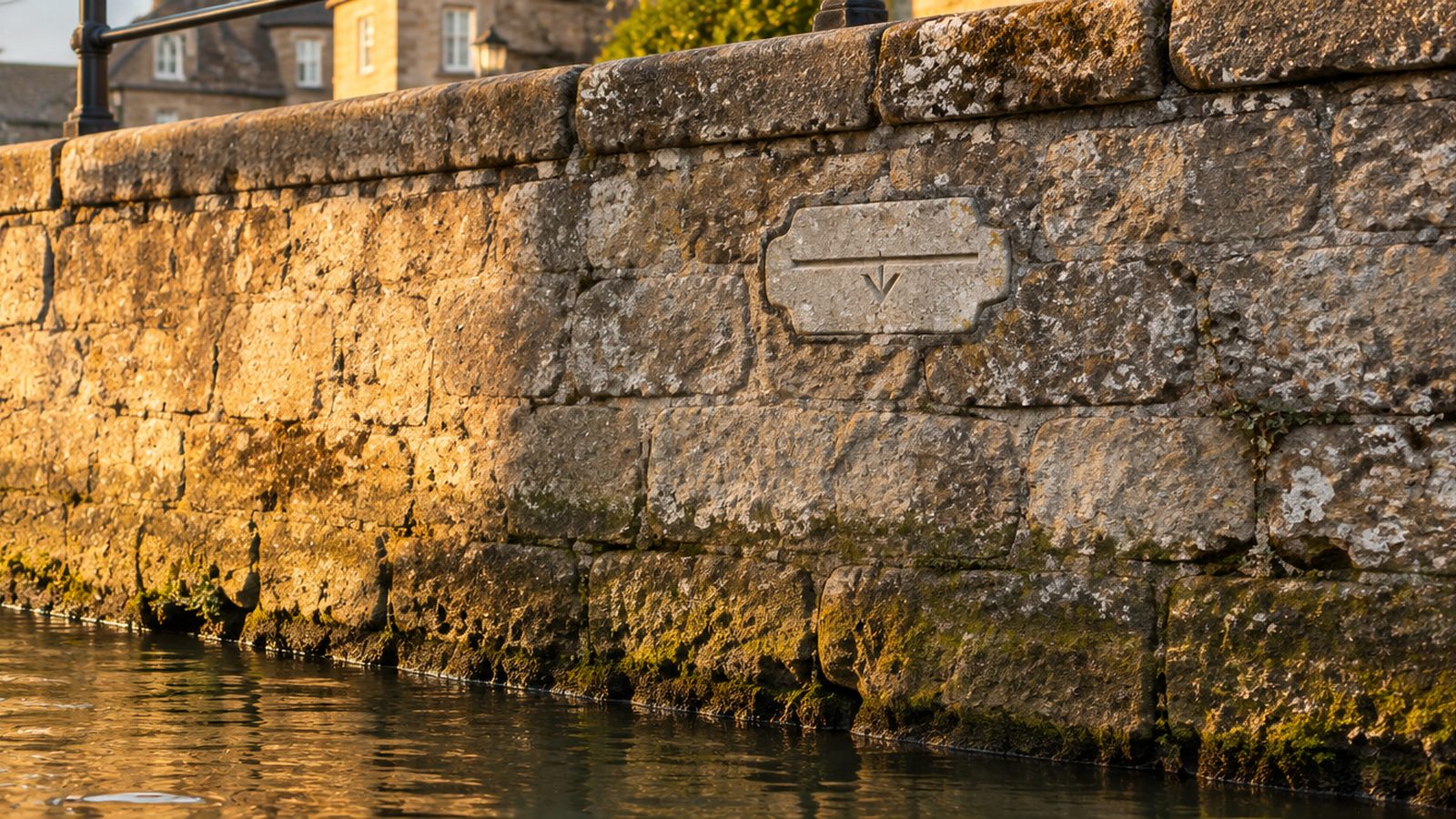 A carved stone high-water mark set into a stone canal wall at the waterline, evening light