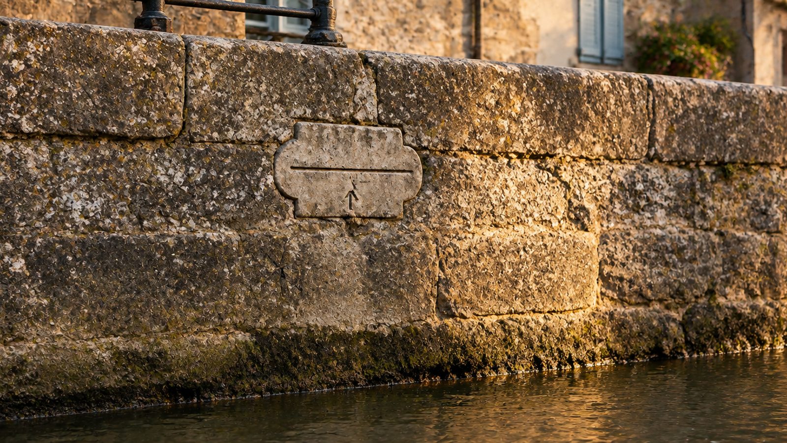 A carved stone high-water mark set into an old canal-side wall, lit by low evening light