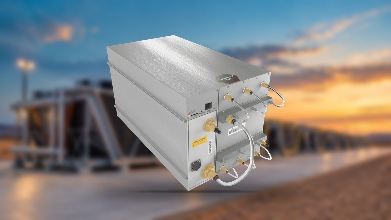 A Bitmain Antminer S21 Hyd in front of a blurred row of dry coolers at dusk
