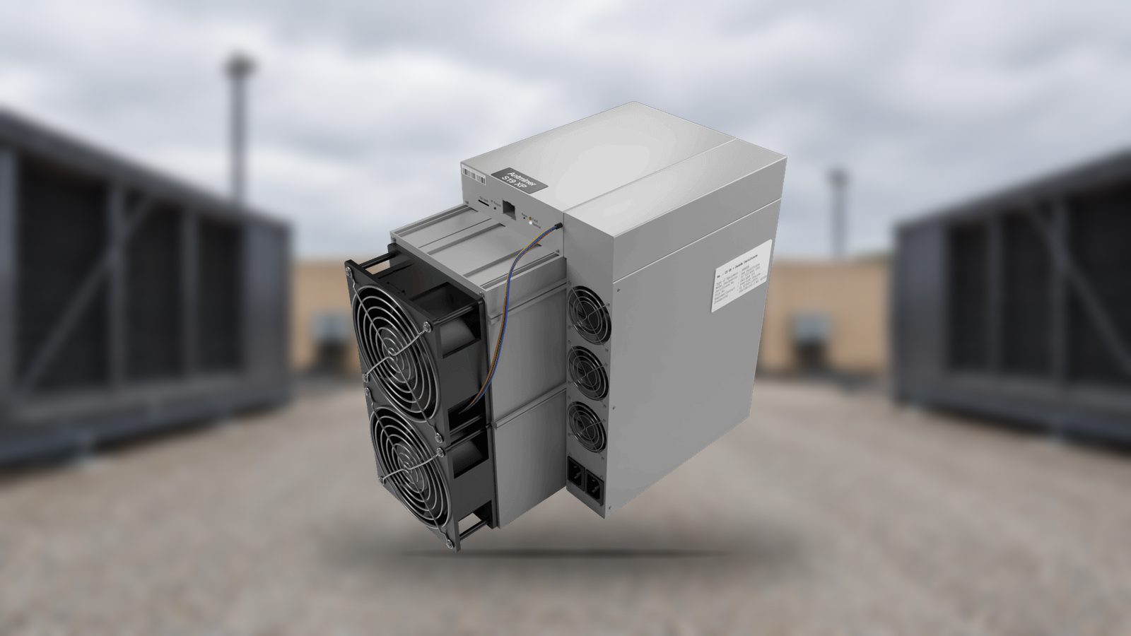 An Antminer S19 XP photographed on a service road between two rows of mining containers, the containers softly out of focus behind it